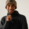 Ein Mann mit brauner Beanie-Mütze und schwarzem Pullover lächelt und hält den Kragen seines Pullovers