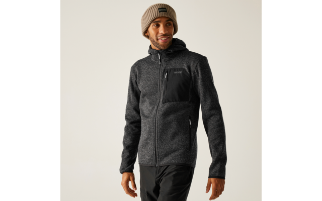 Mann trägt eine schwarze Jacke und eine graue Mütze, steht vor einem hellen Hintergrund