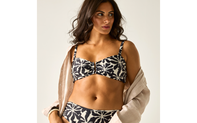 Frau mit dunklen, welligen Haaren trägt schwarz-weiß gemusterten Bikini und helles Hemd über den Schultern, Blick nach rechts