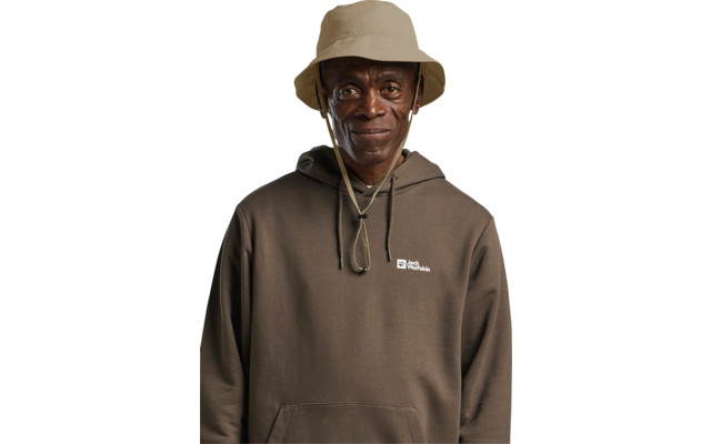 Person, Blick zur Kamera, beige Anglerhut mit Kinnband, brauner Kapuzenpullover mit Bauchtasche und kleinem weißem Logo auf linker Brust
