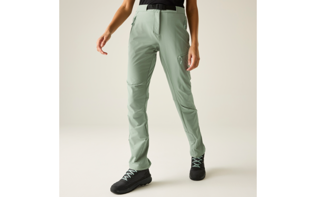 Benedenlichaam in lichtgroene broek met ritszakken, zwarte riem, zwarte schoenen met lichte veters, effen lichte achtergrond