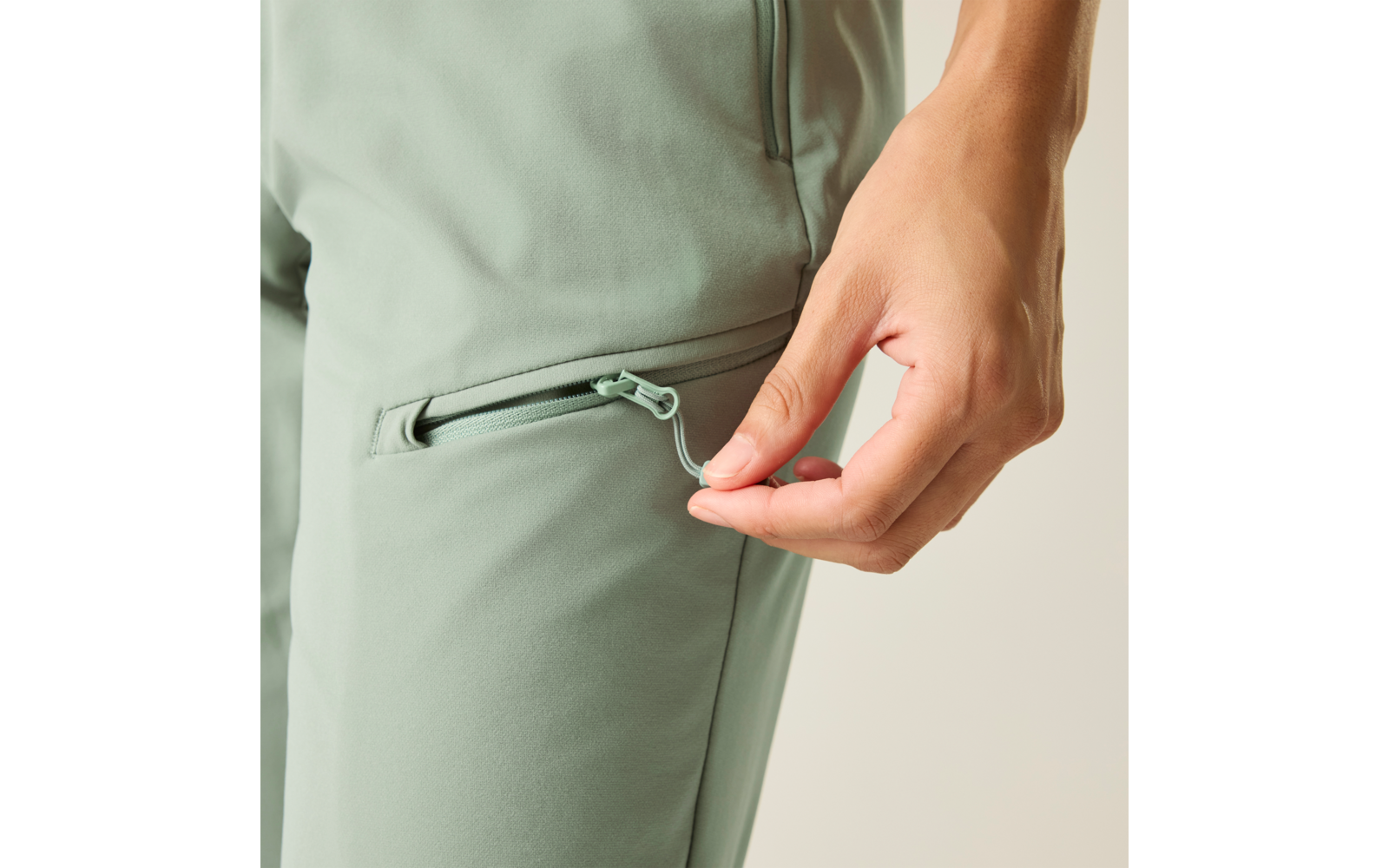 Hand trekt de rits van een zak aan een lichtgroene broek