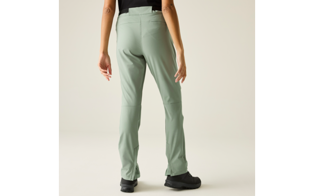 Achteraanzicht van een persoon met lichtgroene broek, zwart bovenstuk en zwarte schoenen, voor een lichte neutrale achtergrond