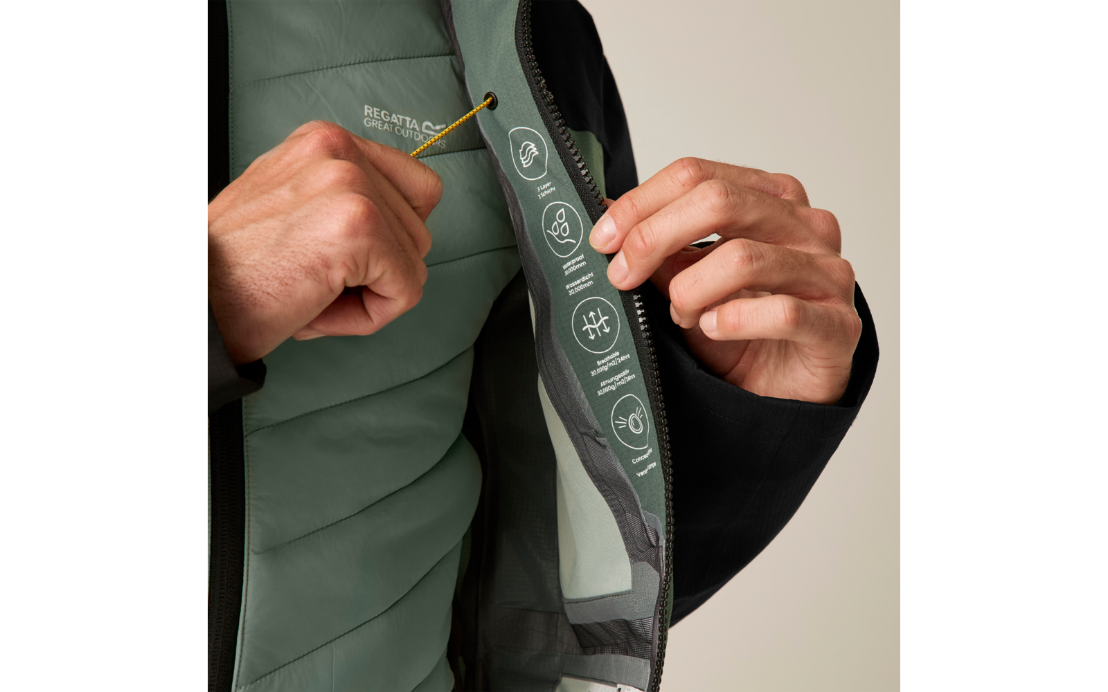 Zwei Hände halten eine schwarze Jacke offen und zeigen das grüne, gesteppte Innenfutter mit weißen aufgedruckten Symbolen, gelbem Kordelzug und Reißverschluss