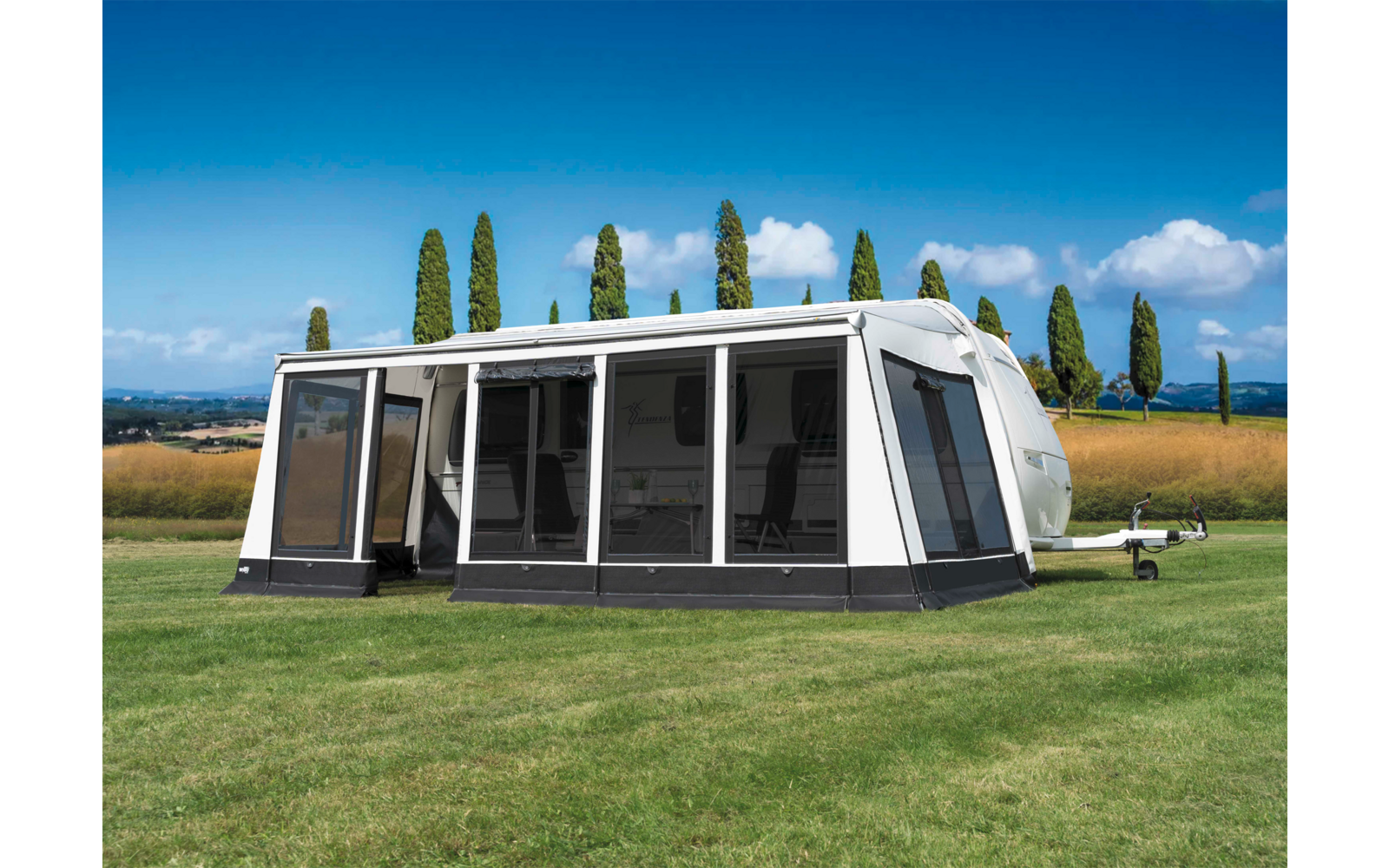 Weißes Wohnwagen-Vorzelt auf grünem Gras mit Bäumen und blauem Himmel im Hintergrund