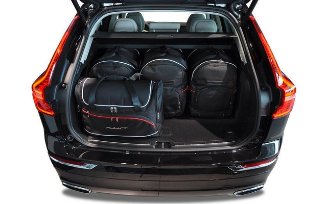Coffre ouvert d'une voiture noire avec cinq sacs de voyage noirs, sièges arrière avec appuie-têtes visibles