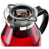 Carafe en verre contenant un liquide rouge, anse noire et infuseur métallique avec feuilles de thé en vrac posé sur l'ouverture