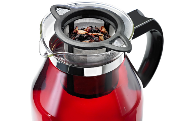 Carafe en verre contenant un liquide rouge, anse noire et infuseur métallique avec feuilles de thé en vrac posé sur l'ouverture