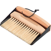 Hand brush with light wooden handle and pale bristles in a black metal dustpan; black hanging strap on the handle
