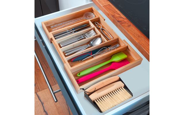 Open kitchen drawer with bamboo organizer holding cutlery, tongs, measuring spoons, two silicone spatulas (green, pink), and small brush
