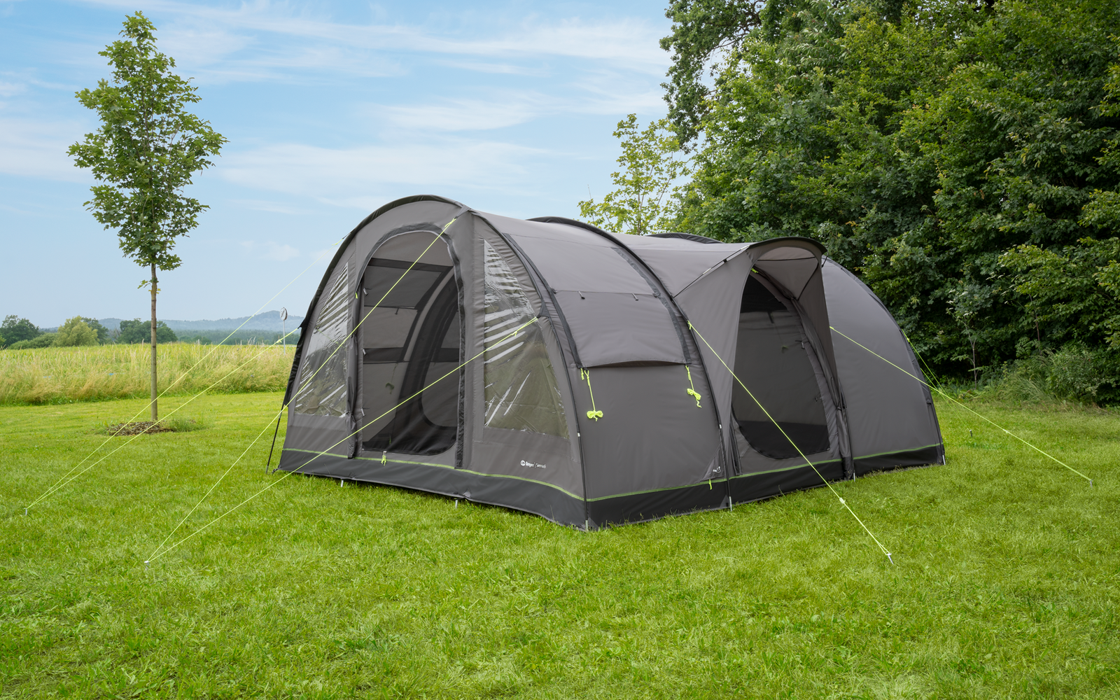 Graues Familienzelt auf einer Wiese unter einem blauen Himmel mit vereinzelten Wolken, umgeben von Bäumen