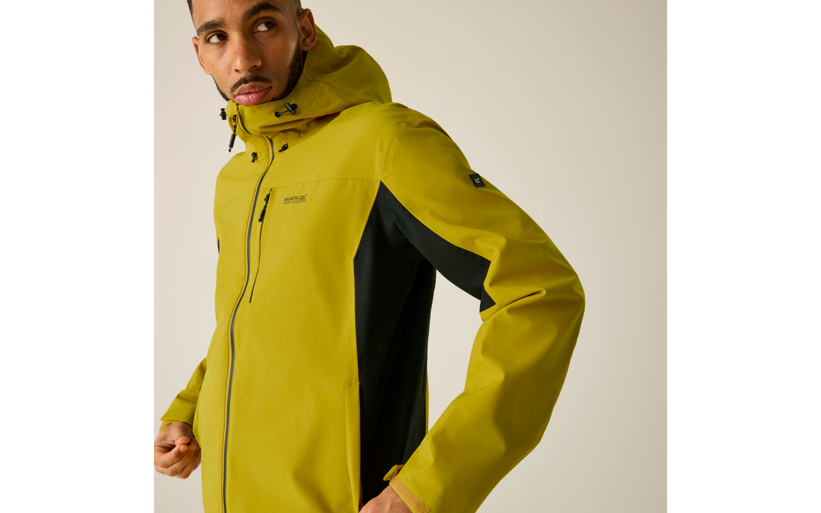 Oberkörper einer Person in gelbgrüner Kapuzenjacke mit schwarzem Seiteneinsatz, Hände am Jackensaum, Blick nach links