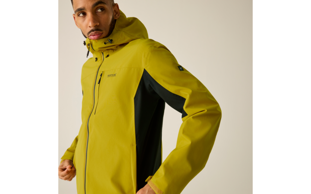 Oberkörper einer Person in gelbgrüner Kapuzenjacke mit schwarzem Seiteneinsatz, Hände am Jackensaum, Blick nach links