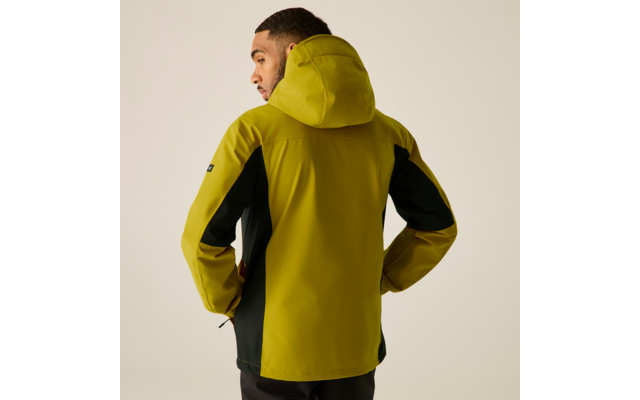 Person von hinten trägt gelbgrüne Kapuzenjacke mit schwarzen Seiteneinsätzen, Hände in den Taschen, heller beiger Hintergrund