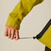 Hand und Unterarm in gelber Jacke halten schwarzen Kordelzug an gelbem Kleidungsstück, Ärmel mit Klettverschluss