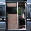 Opengeschoven schuifdeur van een camper met hor; interieur met zitbank, raam en hanglamp