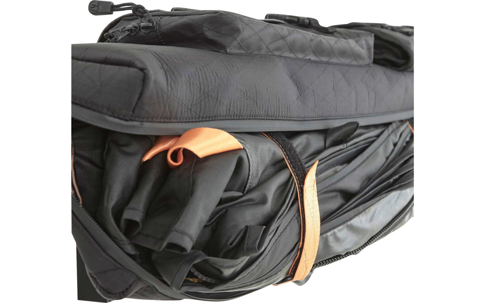 Teilweise geöffnete schwarze Tasche mit gefalteten schwarzen Stofflagen, orangefarbene Schlaufe und Riemen, sichtbarer Reißverschluss und gesteppte Oberfläche