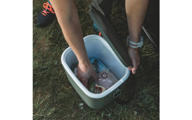 Glacière ouverte sur l'herbe; mains d'une personne saisissent des bouteilles en plastique et une canette; jambes visibles avec baskets et une montre connectée