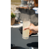 Hand hält ein Glas mit Milch vor einem Tisch im Außenbereich