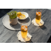 Zwei hohe Gläser mit orangefarbener Flüssigkeit, Eiswürfeln und Limettenscheiben auf hellen, gefransten Untersetzern auf einem dunklen Holztisch; daneben eine runde graue Tischmatte mit einer weißen Schale mit Zitronenscheiben und einer Topfpflanze