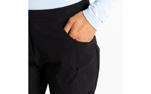 Rechterhand in de voorzak van een zwarte broek, lichtblauw shirt met lange mouwen zichtbaar, witte achtergrond