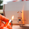 Edelstahlplatte mit der Aufschrift "HIER ZÜNDEN" und "LIGHT HERE", Hand hält orangenes Feuerzeug, kleine Flamme an einer Öffnung