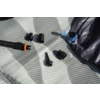 Superficie texturada gris con varias tapas y adaptadores de plástico negro, una manguera corrugada negra con un anillo naranja y una pieza de plástico azul junto a material oscuro doblado