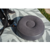 Cojín inflable redondo gris con hendidura central, manguera negra con conector, puntera de zapatilla negra sobre una esterilla gris claro con patrón, hierba en el borde de la imagen