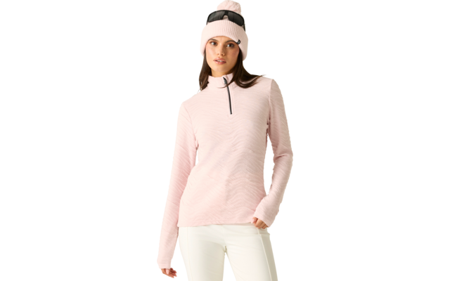 Person mit hellrosa Strickmütze mit Bommel und daraufgelegter Sonnenbrille, hellrosa Langarmpullover mit kurzem Reißverschluss und weißer Hose, steht mit einer Hand in der Tasche