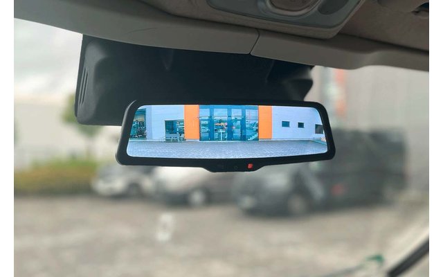 Binnenspiegel van een auto die een gebouw met oranje verticale panelen en blauwe ramen en een parkeerterrein met geparkeerde auto's toont