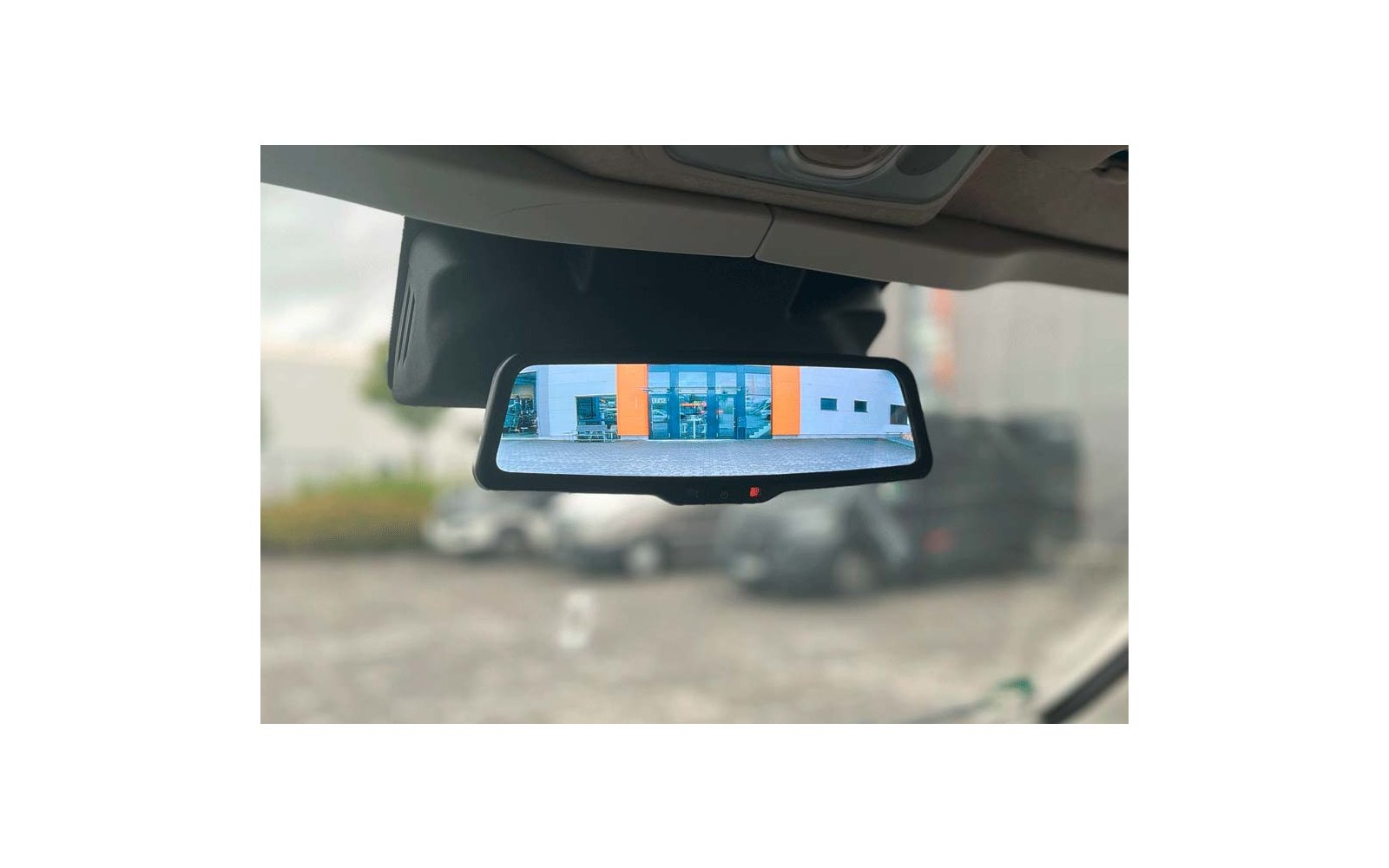 Binnenspiegel van een auto die een gebouw met oranje verticale panelen en blauwe ramen en een parkeerterrein met geparkeerde auto's toont