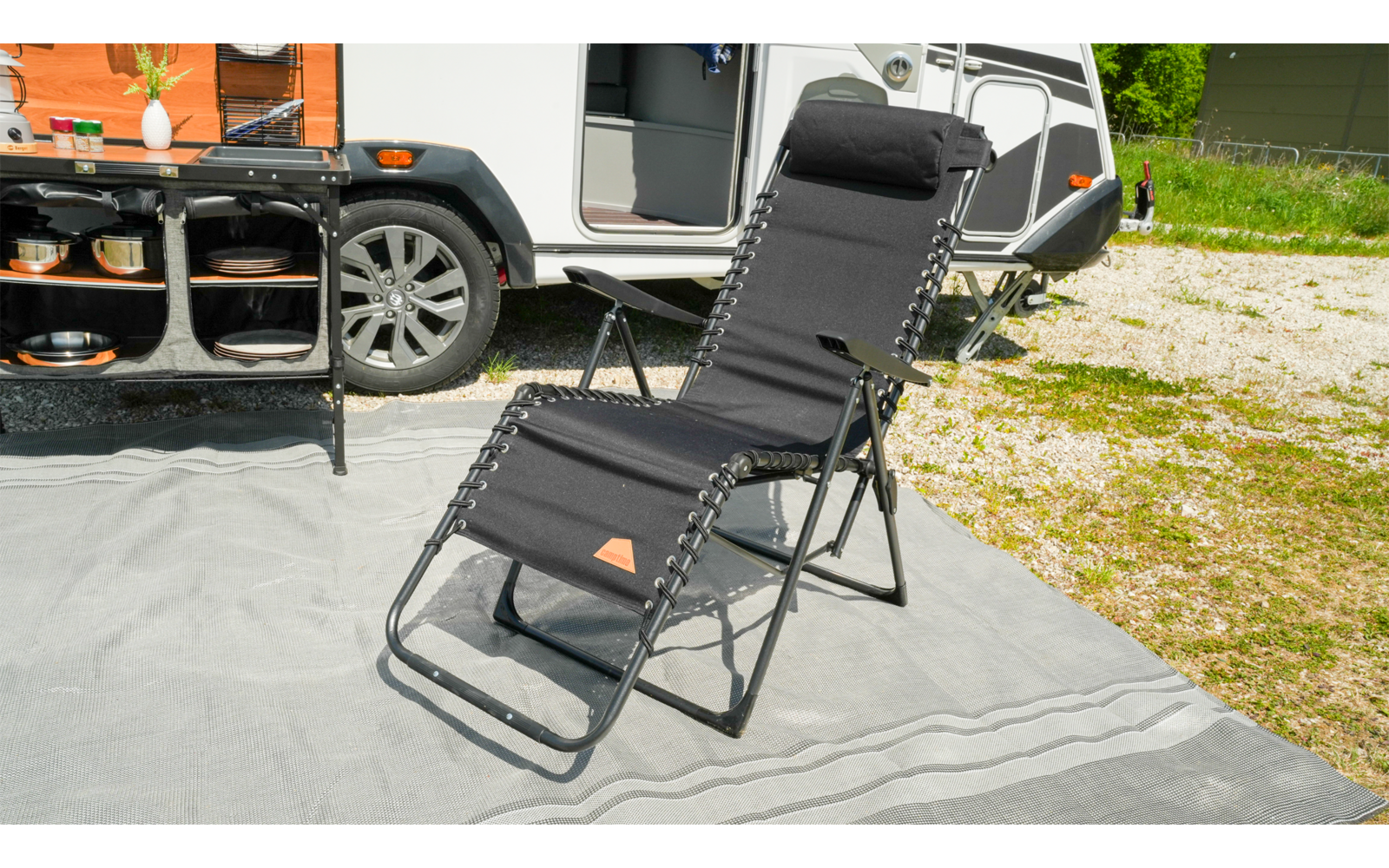 Schwarzer Liegestuhl auf einer grauen Matte neben einem geparkten weißen Wohnmobil
