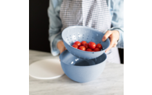 Person hält eine blaue Schüssel mit Kirschtomaten über einer weiteren blauen Schüssel auf einer Arbeitsfläche