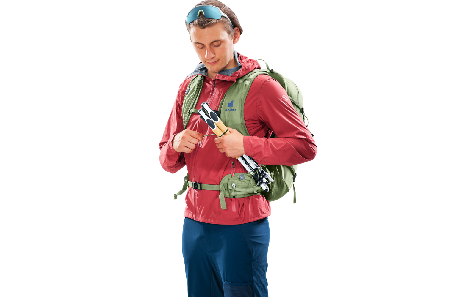 Person in roter Jacke mit grünem Rucksack, Sonnenbrille im Haar, hält eingeklappten Wanderstock