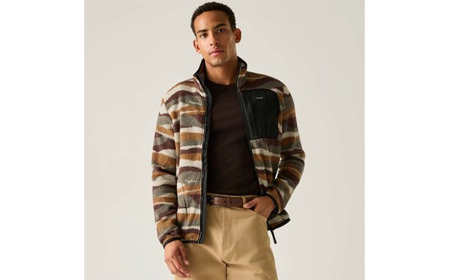 Persoon met een gemêleerd fleecevest met ritssluiting en zwarte borstzak, donker T‑shirt, beige broek en bruine riem, staand voor een lichte achtergrond
