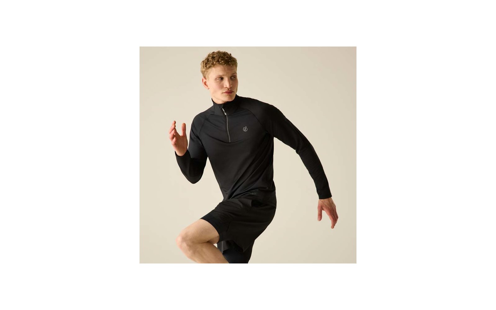 Personne aux cheveux blonds courts portant un haut de sport noir à manches longues et un short noir, pose de course sur fond clair