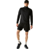 Une personne debout portant une casquette noire, un haut à manches longues noir avec demi-fermeture éclair, un short noir, des chaussettes blanches et des baskets noires