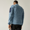 Persoon van achteren in lichtblauw gemêleerd fleecejack met donkerblauwe elleboogpatch op de rechtermouw, zwarte broek, neutrale achtergrond