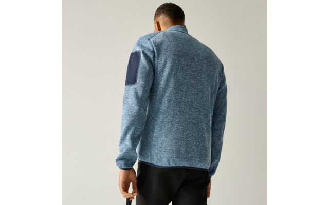 Persoon van achteren in lichtblauw gemêleerd fleecejack met donkerblauwe elleboogpatch op de rechtermouw, zwarte broek, neutrale achtergrond