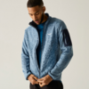 Persoon met kort haar die een lichtblauwe fleecejas met ritssluiting en ritszak op de mouw over een blauw shirt sluit, voor een lichte achtergrond