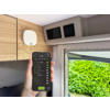 Hand houdt smartphone met een lijst op het scherm; interieur met houten kasten, een wit apparaat aan de wand en geopend raam; groene haag buiten