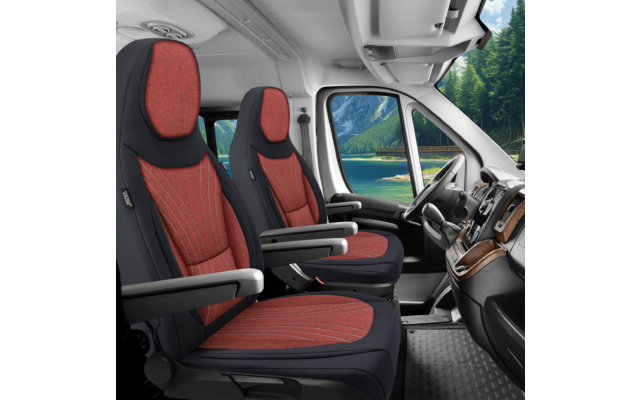 Innenraum eines Fahrzeugs mit zwei roten Vordersitzen, Armlehnen, Lenkrad, Armaturenbrett und durch die Windschutzscheibe sichtbarem See und Bergen