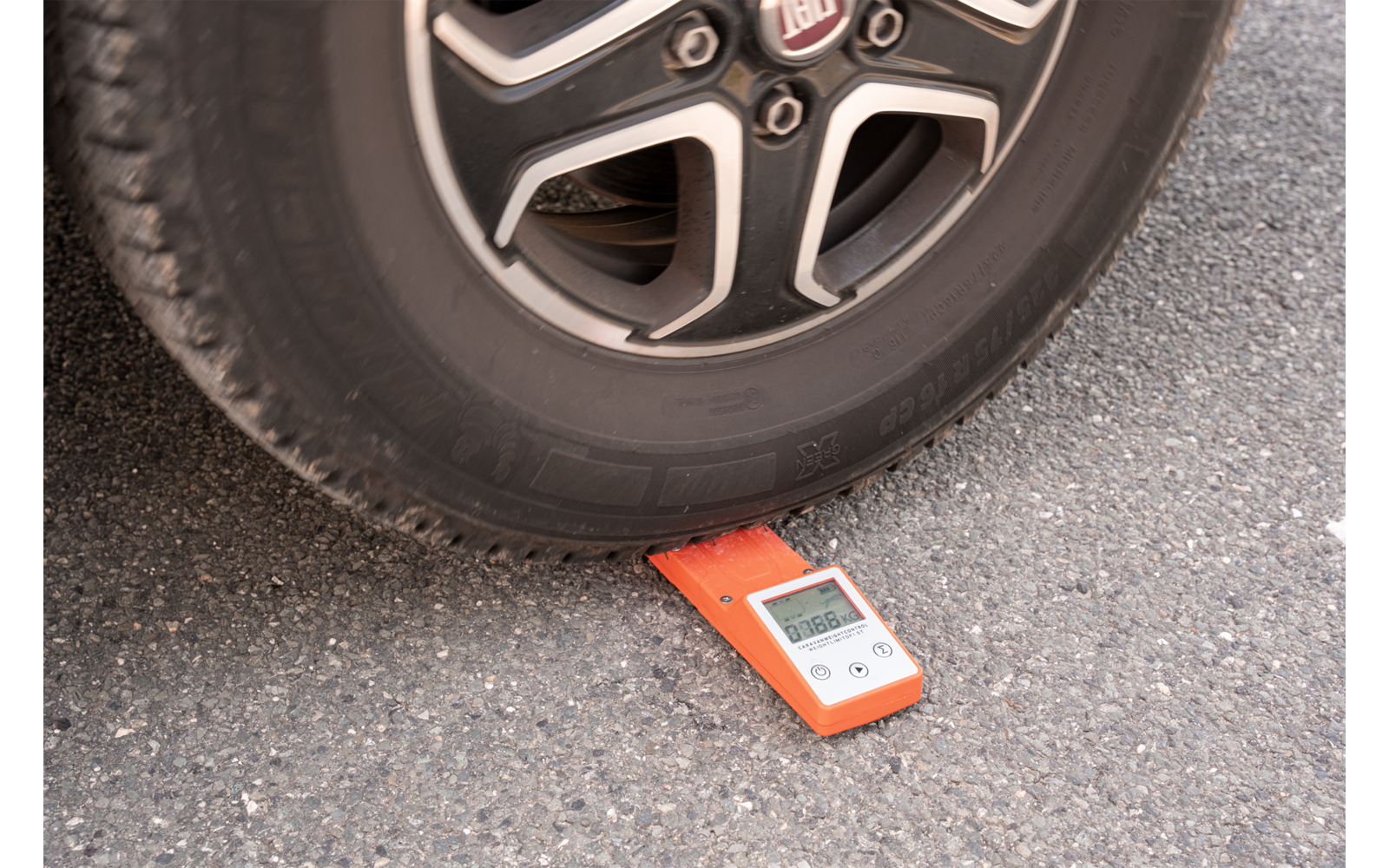 Un dispositivo de medición rojo está en el suelo debajo de una rueda de coche