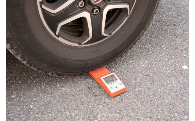 Una rueda de coche está sobre un dispositivo electrónico de medición rojo en el asfalto