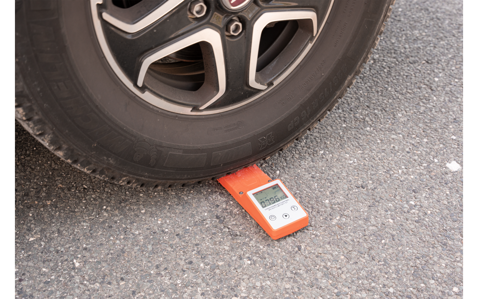 Una rueda de coche está sobre un dispositivo electrónico de medición rojo en el asfalto