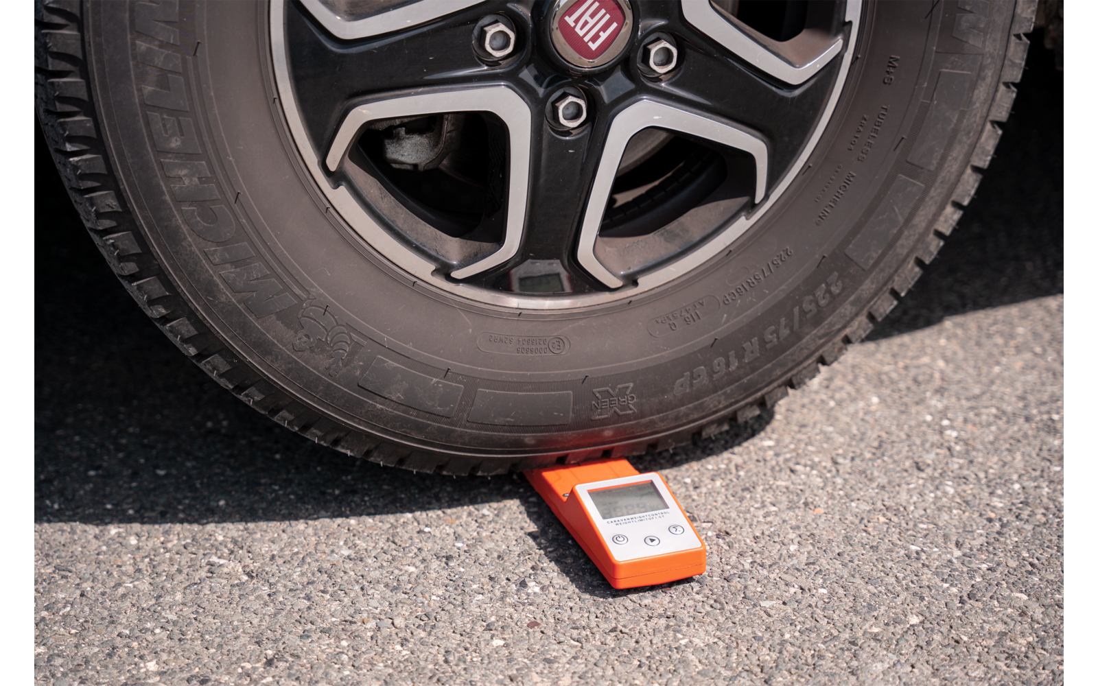 Una rueda de vehículo está sobre un dispositivo de medición naranja sobre el asfalto