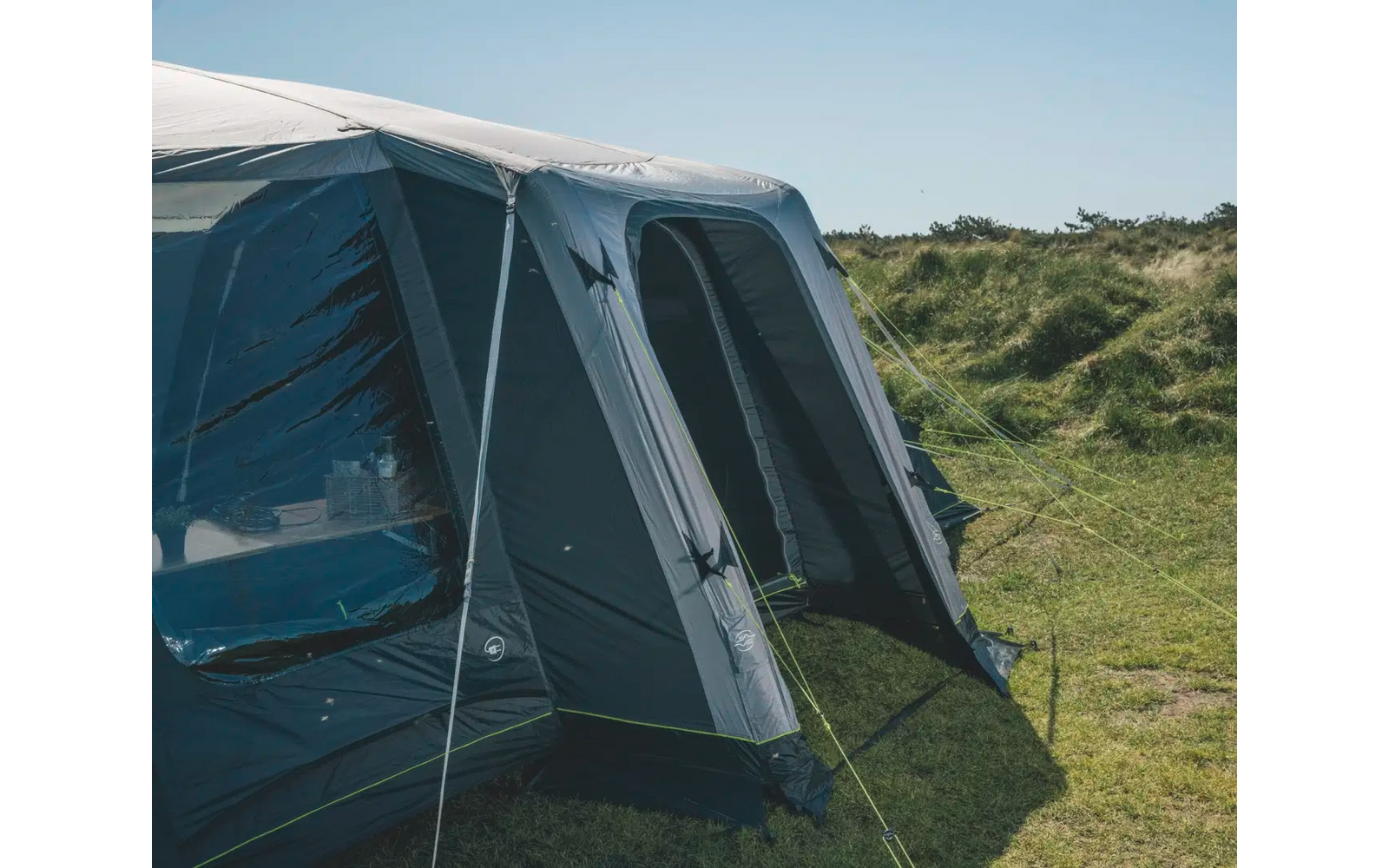 Großes blaues und graues Zelt steht auf einer grünen Wiese bei sonnigem Himmel