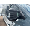 Nahaufnahme eines seitlichen Außenspiegels an einem grauen Wohnmobil mit schwarzer Spiegelabdeckung; weitere Wohnmobile und bewölkter Himmel im Hintergrund
