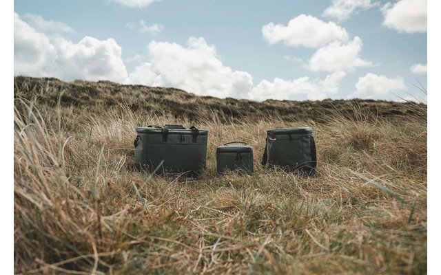 Tres cajas rectangulares verdes sobre la hierba frente a dunas, cielo parcialmente nublado