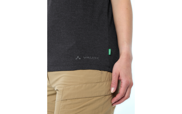 Unterer Torso einer Person: dunkelgraues T‑Shirt mit VAUDE-Logo und grünem Etikett am Saum, rechte Hand mit weißen Fingernägeln an hellbrauner Cargohose